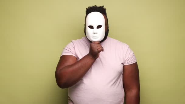 身穿粉色T恤的非裔美国人戴着面具 性格和情绪不断变化 面部表情和情绪各不相同 室内拍摄被隔离在浅绿色背景下 — 图库视频影像