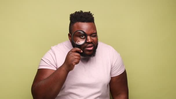 재밌는 아프리카 미국인 분홍색 티셔츠를 돋보기를 긍정적 얼굴로 스튜디오는 배경에 — 비디오