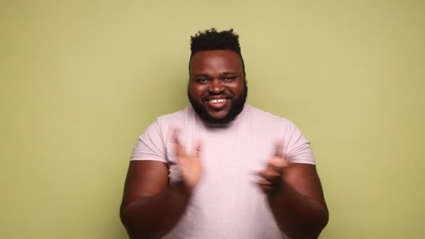 喜びに満ちた陽気な髭を生やしたアフリカ系アメリカ人男性がピンクのTシャツを身に着けて拍手を送り パフォーマンスに拍手を送り 幸せそうに見えます ブラボー 薄い緑の背景に隔離された屋内スタジオショット — ストック動画
