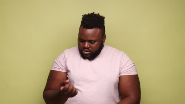 不幸な病気のひげを生やしたアフリカ系アメリカ人の男性は 痛みを伴う手に触れるピンクのTシャツを着て 捻挫手首 痛みを感じている 薄い緑の背景に隔離された屋内スタジオショット — ストック動画