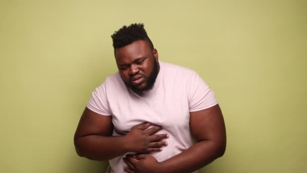 胃の痛みや食事の問題 ピンクのTシャツを着たアフリカ系アメリカ人の病気の男性が立って 彼の痛みを伴う腹を保持し 悪い感じ 薄い緑の背景に隔離された屋内スタジオショット — ストック動画