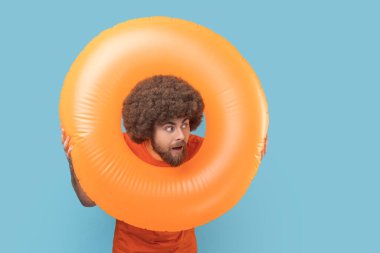 Şaşırmış yüz ifadesine sahip bir adamın portresi parlak turuncu kauçuk halkalardan uzak, tatilimize şaşırmış bir şekilde. Mavi arka planda kapalı stüdyo çekimi.