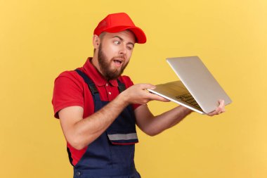 Mavi üniformalı ve kırmızı şapkalı sakallı bir işçinin portresi. Elinde yarı açık defter, casusluk ve yasak bilgi var. Sarı arka planda kapalı stüdyo çekimleri.