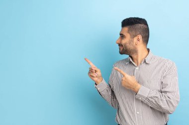 Gülümseyen sakallı işadamı, fikir sunumu için boş fotokopi alanı gösteriyor, ticari metin, başka yöne bakıyor, çizgili gömlek giyiyor. Mavi arka planda kapalı stüdyo çekimi.