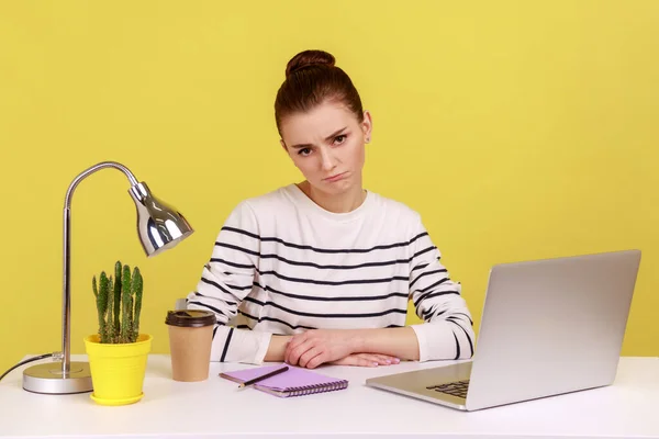 闷闷不乐的女经理穿着条纹衬衫坐在工作场所看着镜头 厌倦了网上会议 在黄色背景下隔离的室内工作室拍摄 — 图库照片