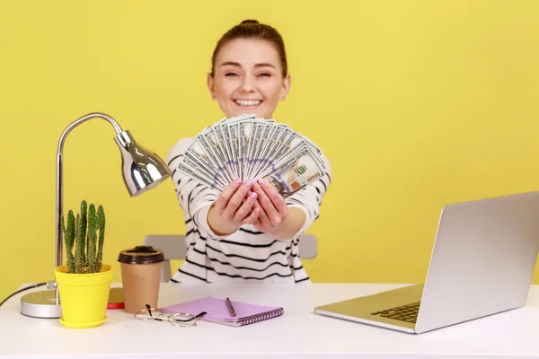 快乐的富有女性办公室经理 手里拿着100美元的钞票 坐在工作场所 对丰厚的利润感到满意 在黄色背景下隔离的室内工作室拍摄 — 图库照片