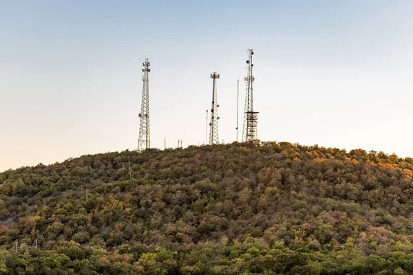 森の背景を持つ光の青空と丘の上の通信アンテナ — ストック写真
