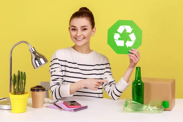 リサイクルサインを保持し 緑を考え プラスチック ガラス瓶や段ボールパッケージを指している楽しい女性のオフィスマネージャー 黄色の背景に隔離された屋内スタジオショット — ストック写真
