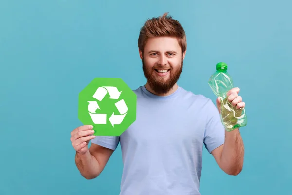 面带微笑的英俊英俊大胡子男人的画像手握瓶子回收标牌 塑料处理 垃圾处理 室内拍摄被蓝色背景隔离 — 图库照片