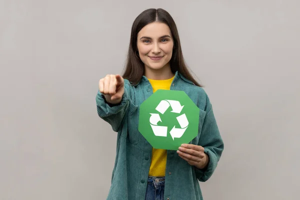 ゴミを整理しろ 環境を心配し カジュアルなスタイルのジャケットを着て カメラで指を指してリサイクル標識を保持楽観的な女性 灰色の背景に隔離された屋内スタジオショット — ストック写真