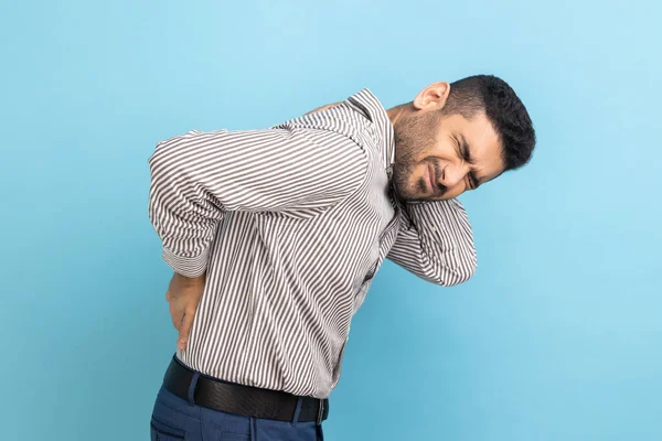 背痛或脊柱或肾痛 年轻生病的商人穿着条纹衬衫 站在那里摸着背 感到疼痛的画像 室内拍摄被蓝色背景隔离 — 图库照片