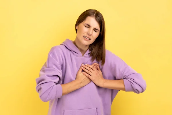 突然の心臓発作 心筋梗塞 乳がんのリスク 紫色のパーカーを身に着けている苦しみを眉をひそめて過労うつ病女性の肖像画 黄色の背景に隔離された屋内スタジオショット — ストック写真