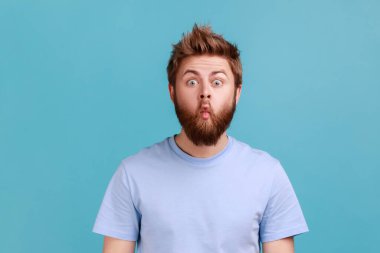 Portrait of funny comic face handsome bearded man standing with fish lips and looking at camera, childish behavior, having fun, good mood. Indoor studio shot isolated on blue background.