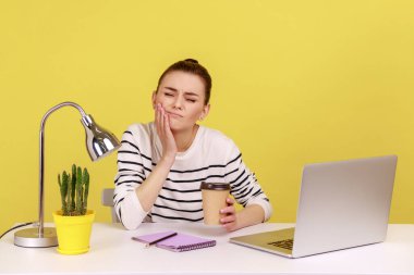 Unhappy woman office worker touching cheek with fingers feeling unpleasant toothache after drinking hot coffee, dentistry problems. Indoor studio studio shot isolated on yellow background.