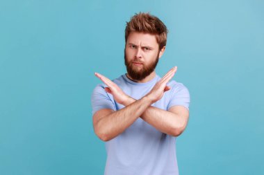 There is no way. Portrait of concerned disappointed handsome bearded man showing x sign with crossed hands, meaning stop, finish. Indoor studio shot isolated on blue background.