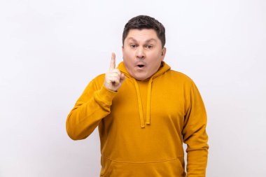 Portrait of clever smiling middle aged man pointing finger up, has good idea genius plan, inspiration and creativity, wearing urban style hoodie. Indoor studio shot isolated on white background.