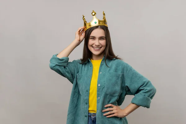 Woman in crown on head looking at with confident expression, self-motivation and dreams to be best. keeping hand on hip, wearing casual style jacket. Indoor studio shot isolated on gray background.