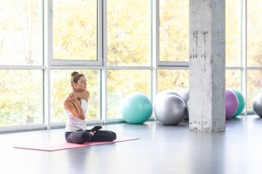 Portrait of calm relaxed woman stretching her arms, doing exercise and easy yoga, keeps eyes closed, Improving her health by extending meditating. Indoor shot with window on background.