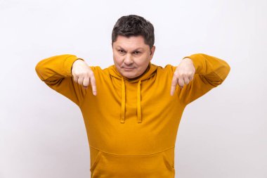 Come to me here now. Man pointing fingers down, demanding approach to him immediately, having control over situation, wearing urban style hoodie. Indoor studio shot isolated on white background.