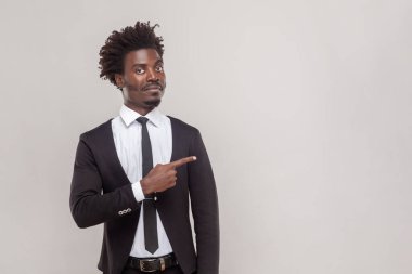 Portrait of man with petit goatee showing free space for your advertising content or promotional text, wearing white shirt and tuxedo. Indoor studio shot isolated on gray background.