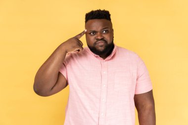 Crazy idea. Portrait of man in pink shirt showing stupid gesture, looking at camera with condemnation and blaming for insane plan, dumb suggestion. Indoor studio shot isolated on yellow background.