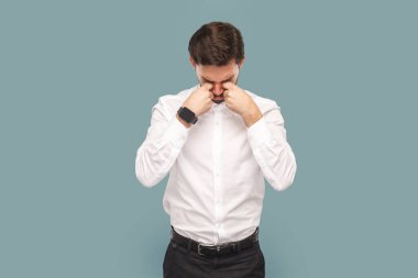 Portrait of sad depressed crying man with mustache standing and rubbing his eyes, being in bad mood and having stress, wearing Indoor studio shot isolated on light blue background.