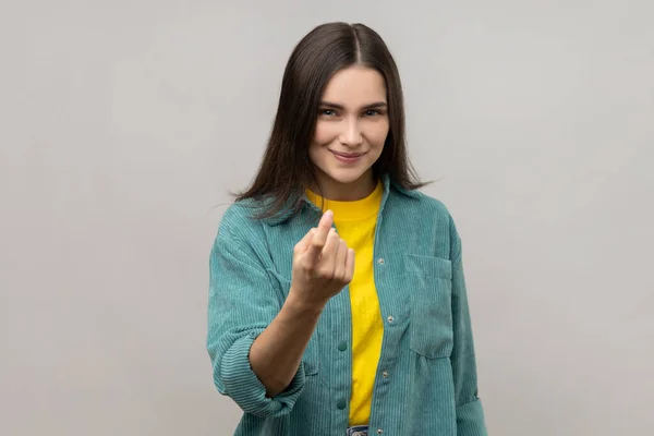 Come here. Portrait of attractive woman gesturing come to me, beckoning with finger, inviting for confidential talk, wearing casual style jacket. Indoor studio shot isolated on gray background.