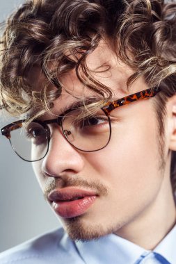 Yakından bakınca, bıyıklı, mavi gömlekli, kıvırcık saçlı, ciddi bir yüz ifadesiyle yüzünü çeviren yakışıklı, katı bir adamın portresi. Gri arka planda izole edilmiş kapalı stüdyo görüntüleri.