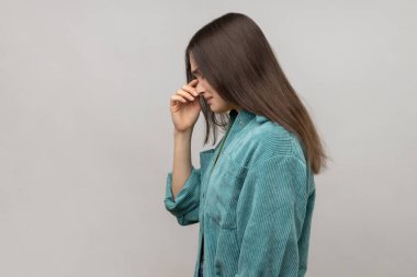 Depresif bir kadının başını eğip, yüzüne dokunup, suratını buruşturarak ağlaması, üzüntü duyması, günlük tarz ceket giymesi. Gri arka planda izole edilmiş kapalı stüdyo görüntüleri.