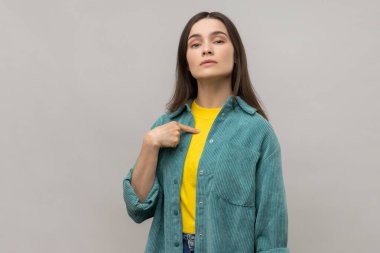 Kendine güvenen egoist bir kadın kendini kibirli ve tatmin edici bir şekilde gösteriyor, kendisiyle gurur duyuyor, başarılarıyla övünüyor, günlük tarz ceket giyiyor. Gri arka planda izole edilmiş kapalı stüdyo görüntüleri.