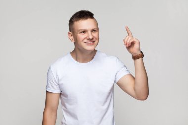 Evreka. Yakışıklı, heyecanlı, tişört giyen, parmağını kaldırmış, harika bir fikri olan ve gülümseyen genç çocuğun portresi. Gri arka planda izole edilmiş kapalı stüdyo görüntüleri.