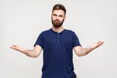 Please, take for free. Kind generous man in dark T-shirt outstretching hands as if giving for free, offering to embrace, inviting with hospitable expression. Indoor shot isolated on gray background. clipart