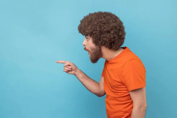 侧视图非洲式发型的男人在橙色T恤指向一边 显示空白副本空间的想法介绍 商业广告文本 展望未来 室内拍摄被蓝色背景隔离 — 图库照片