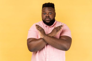 Hayatta olmaz, kesinlikle olmaz. Pembe tişört giyen, x işaretini çapraz elle gösteren bir adamın portresi. Yani dur, bu son. Sarı arka planda kapalı stüdyo çekimleri.