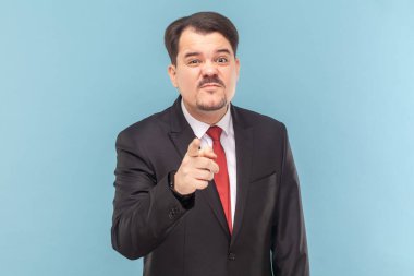 Bıyıklı üzgün adamın portresi sana bakıyor, suratını asmış kameraya bakıyor, siyah takım elbise ve kırmızı kravat takıyor. Açık mavi arkaplanda izole edilmiş kapalı stüdyo çekimi.