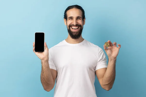 Sakallı Beyaz Tişörtlü Gülümseyen Elinde Cep Telefonu Altın Bitcoin Olan — Stok fotoğraf