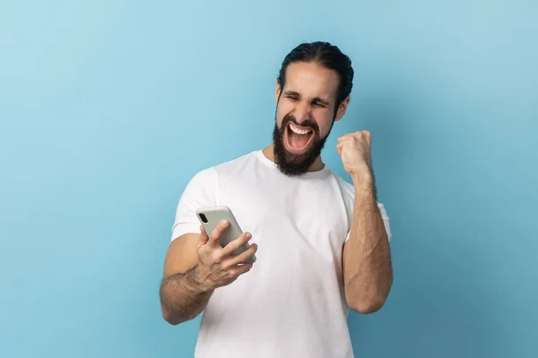 Sakallı Beyaz Tişörtlü Cep Telefonu Kullanan Yumruğunu Sıkan Bahis Oynayan — Stok fotoğraf