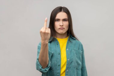 Koyu renk saçlı kadının iletişimi reddetmesi, saygısızlığı ve nefreti ifade etmek için orta parmağını göstermesi, kaba bir jest, günlük tarz ceket giymesi. Gri arka planda izole edilmiş kapalı stüdyo görüntüleri