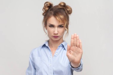 Burada dur. Sarışın bir kadının portresi, uzanmış elleriyle, yasaklama jesti yapıyor, bir şeyi yasaklıyor, mavi gömlek giyiyor. Gri arka planda izole edilmiş kapalı stüdyo görüntüleri.