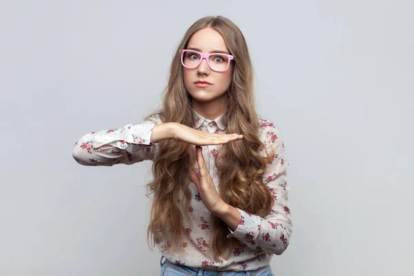 I need more time, enough limits. Woman in glasses with long hair showing time out hand gesture, looking imploringly, worried about deadline. Indoor studio shot isolated on gray background.