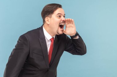 Bıyıklı öfkeli adamın dikilip yüksek sesle bağırması, elini ağzının yakınında tutması, kırmızı kravatlı siyah takım elbise giymesi. Açık mavi arkaplanda izole edilmiş kapalı stüdyo çekimi.