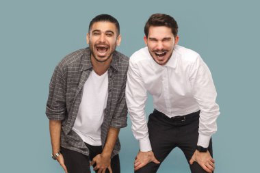 Çok mutlu iki gülen adamın portresi. Kameraya bakıyorlar. Çok komik bir şey görüyorlar. Açık mavi arkaplanda izole edilmiş kapalı stüdyo çekimi.