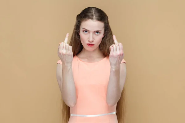 Portrait of rude impolite attractive pretty woman with long hair showing middle finger, arguing with somebody, wearing elegant dress. Indoor studio shot isolated on brown background.