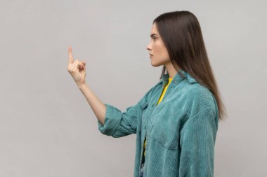 Koyu renk saçlı kadının iletişimi reddetmesi, saygısızlığını göstermek için orta parmağını göstermesi ve kaba hareketlerden nefret etmesi, günlük tarz ceket giymesi. Gri arka planda izole edilmiş kapalı stüdyo görüntüleri