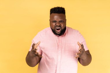 Pembe tişört giyen sinirli agresif bir adamın portresi kollarını kaldırmış, saldırganlığını, bağırışlarını, kaşlarını çatık suratını ifade ediyor. Sarı arka planda kapalı stüdyo çekimleri.