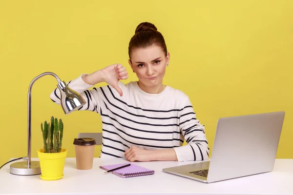 不高兴的办公室女职员表现出低垂的大拇指 不喜欢的手势 表示不赞成 批评与笔记本电脑一起坐在工作场所 在黄色背景下隔离的室内工作室拍摄 — 图库照片