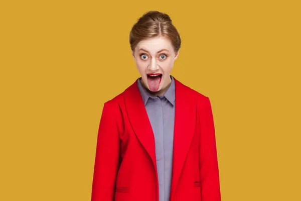 赤い唇を持つ女性の肖像画は舌を突き出し 幸せな優雅さを作り 長い髪をしており 肯定的な感情を表現し 赤いジャケットを着ている 黄色の背景に隔離された屋内スタジオショット — ストック写真