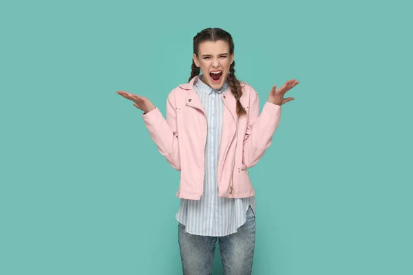 一个身穿粉色夹克 头戴辫子 怒气冲冲的少女的画像 高举双臂 带着憎恨尖叫 室内拍摄被绿色背景隔离 — 图库照片