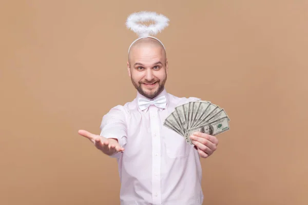 满意的富有的秃头男人的画像 头戴灵巧的头巾 露出美元钞票 给你薪水 穿着浅粉色衬衫 打着领结 在棕色背景下被隔离的室内拍摄 — 图库照片