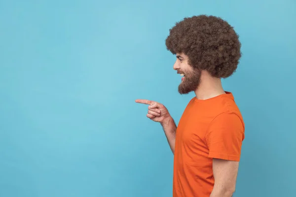 从侧面看 黑人发型的男人穿着橙色的T恤 指尖着手指 脸上挂着灿烂的微笑 为你的广告空出了空间 室内拍摄被蓝色背景隔离 — 图库照片